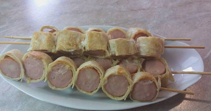 Sausages in pita bread with cheese on skewers in a pan